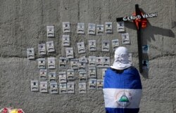 A demonstrator wearing the national flag looks at pictures of protesters who died during the protests against Nicaraguan President Daniel Ortega's government last year, in Managua, Nov. 2, 2019.