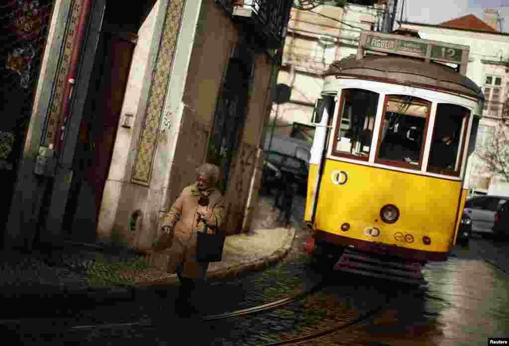 A woman walks near a tram at the Alfama neighborhood in Lisbon, Portugal. 