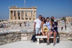 FILE - A French family poses in front of the ancient Parthenon, at the Acropolis Hill, during a hot day in Athens, July 31, 2020.