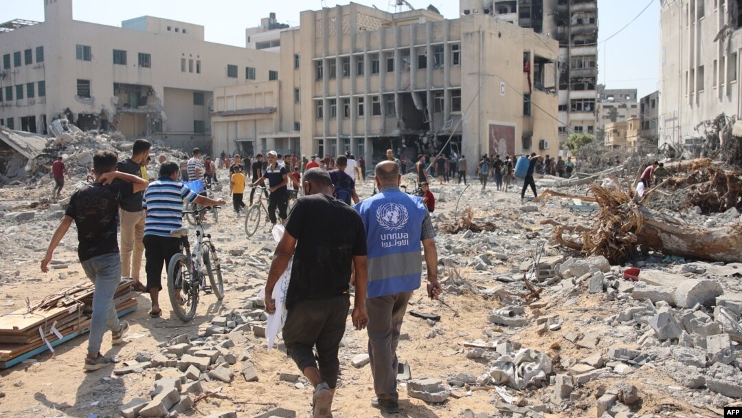 Orang-orang berjalan di tengah puing-puing bangunan Badan Bantuan dan Pekerjaan PBB yang menangani pengungsi Palestina di kawasan Al-Sinaa setelah pasukan Israel mundur di Kota Gaza, Jumat, 12 Juli 2024. (Foto: Al-Qattaa/AFP)