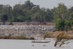 FILE - A fishing boat passes near a construction site of a dam, near Cambodia-Laos borders, in Preah Romkel village, Stung Treng province, northeast of Phnom Penh, Cambodia, June 20, 2016.