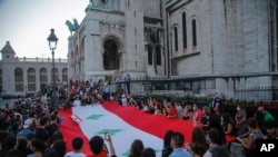 Members of the Lebanese community hold a giant Lebanese flag during a vigil in memory of victims of the deadly blast in Beirut, in front of Sacre Coeur Basilica in Paris, France, Aug. 5, 2020. 