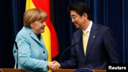 Germany's Chancellor Angela Merkel (L) shakes hands with Japan's Prime Minister Shinzo Abe
