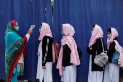 FILE - Students wear protective masks as they have their temperature checked before entering classrooms as secondary schools reopen amid the second wave of the coronavirus disease (COVID-19) outbreak, in Peshawar, Pakistan, Jan. 18, 2021.