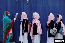 FILE - Students wear protective masks as they have their temperature checked before entering classrooms as secondary schools reopen amid the second wave of the coronavirus disease (COVID-19) outbreak, in Peshawar, Pakistan, Jan. 18, 2021.