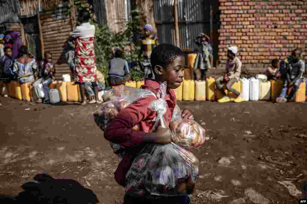 A boy sells snacks as residents queue with their water jars to collect water from a water point in Bukavu, Democratic Republic of Congo.