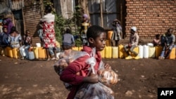 A boy sells snacks as residents queue with their water jars to collect water from a water point in Bukavu, Democratic Republic of Congo.