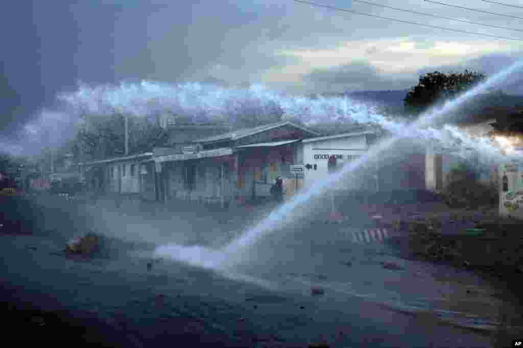 A police officer keeps an eye on demonstrators as a water canon clears barricades in the Nyakabyga district of Bujumbura, Burundi. Days of deadly clashes have rocked Burundi since the ruling party nominated President Pierre Nkurunziza to stand for reelection on April 25 for a potential third term in office.