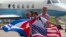 FILE - Passengers of JetBlue Flight 387 holding U.S. and Cuban flags pose for photos in front of the plane transporting U.S. Transportation Secretary Anthony Foxx, at the airport in Santa Clara, Cuba, Aug. 31, 2016.