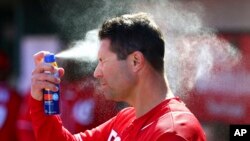 FILE - Cincinnati Reds third base/catching coach J.R. House applies sunscreen to his face while in the dugout during the third inning of a spring training baseball game against the Cleveland Indians Saturday, Feb. 23, 2019, in Goodyear, Ariz. (AP Photo/Ro