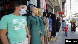 A vendor wearing a face mask stands in front of his school uniform shop, ahead of the first day of the new school year, amid fears of rising number of the COVID-19 cases in Amman, Jordan, Aug. 31, 2020.