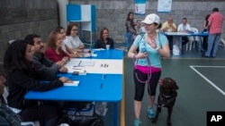 A woman waves to polling officers as she walks with her dog after casting her vote in Guatemala City, Guatemala, Aug. 11, 2019.