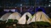 FILE - A migrant sits in his tent during the evacuation of a makeshift camp set up near the La Porte d'Aubervilliers in Paris, France, Jan. 28, 2020. 