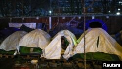 FILE - A migrant sits in his tent during the evacuation of a makeshift camp set up near the La Porte d'Aubervilliers in Paris, France, Jan. 28, 2020. 