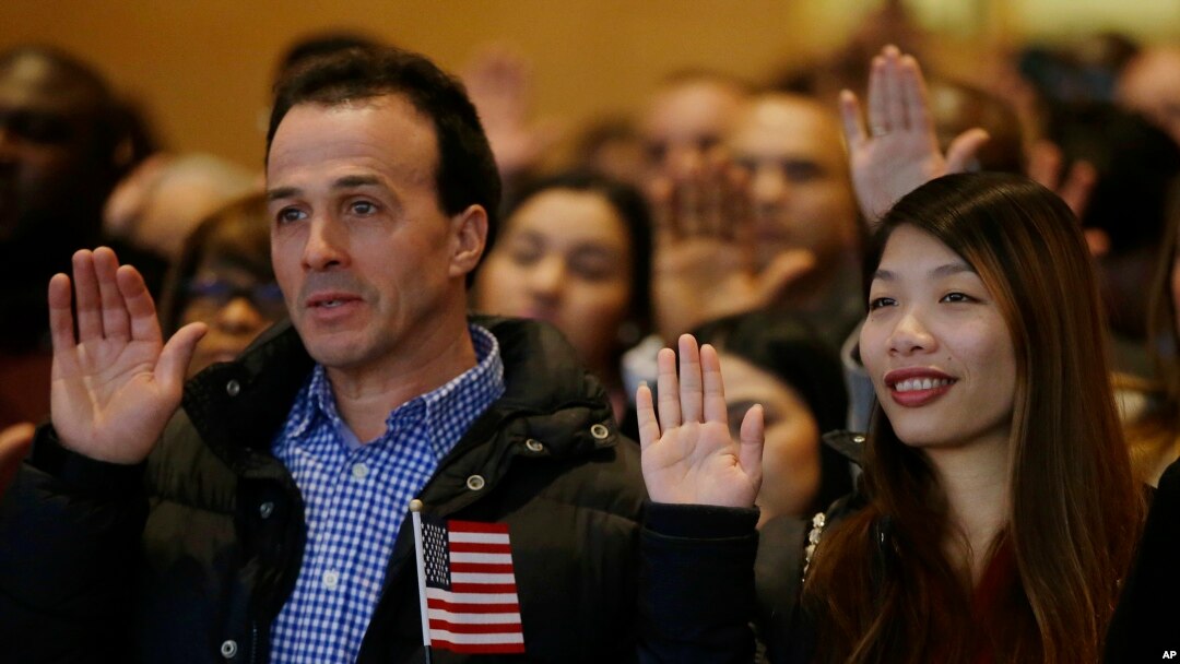 Weizhen Cai from China, right, and Ahmed Haloui from Morocco recite the oath of citizenship during a celebration of the naturalization off approximately 200 new citizens of the United States, Nov. 30, 2017 at the John F. Kennedy Library in Boston.