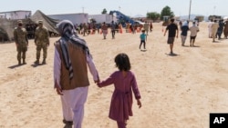 ARCHIVO - Un hombre camina con un niño por la aldea Doña Ana de Fort Bliss, donde se alojaban refugiados afganos, en Nuevo México, el 10 de septiembre de 2021.