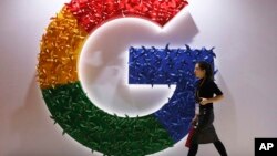 In this Monday, Nov. 5, 2018 file photo, a woman walks past the logo for Google at the China International Import Expo in Shanghai. (AP Photo/Ng Han Guan, File)