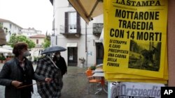 People stand in front of a newsstand displaying a daily headline reading in Italian " Mottarone, tragedy with 14 dead," in Stresa, northern Italy, May 24, 2021.