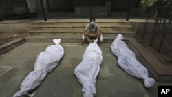 FILE - In this April 20, 2021, file photo, a man waits for the cremation of a relative who died of COVID-19, placed near bodies of other victims, in New Delhi, India. India’s death toll from COVID-19 has surpassed 200,000 as a virus surge sweeps the count