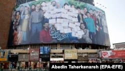 IRAN -- An Iranian couple drives past a huge election billboard in Vali-Asr square in Tehran, June 17, 2021