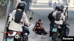 FILE – Venezuelan security forces pause near opposition supporters affected by tear gas during a demonstration in Caracas, July 9. A new Amnesty International report condemns 'illegal home raids' against suspected dissidents. 