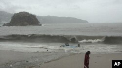 A person walks past an upturned car by the shore after the vehicle was swept into the ocean by high waves caused by the approach of Tropical Storm Beatriz in Acapulco, June 20, 2011