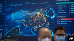 FILE - Visitors wearing face masks stand near a display showing an electronic map of China at the PT Expo in Beijing, June 4, 2023. The annual expo showcases Chinese and foreign technology firms.