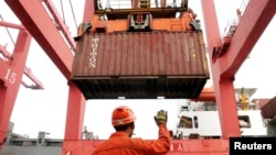 FILE PHOTO: An employee guides as a crane unloads shipping containers from a cargo ship at a port in Lianyungang, Jiangsu province, China, March 8, 2014. 