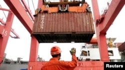 FILE PHOTO: An employee guides as a crane unloads shipping containers from a cargo ship at a port in Lianyungang, Jiangsu province, China, March 8, 2014. 