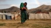 Internally displaced Afghan girl carries a child near their shelter at a refugee camp