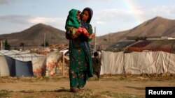 Seorang gadis pengungsi Afghanistan menggendong anak di dekat tenda pengungsian di luar kota Kabul, Afghanistan, 20 Juni 2019. (Foto: Reuters/Omar Sobhani)