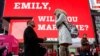 Joe lodato (kiri) meminang pacarnya, Emily Gambarella pada Hari Valentine (14/2), seperti juga tertulis di layar iklan: Emily, maukah menikah denganku?, di Times Square, New York.