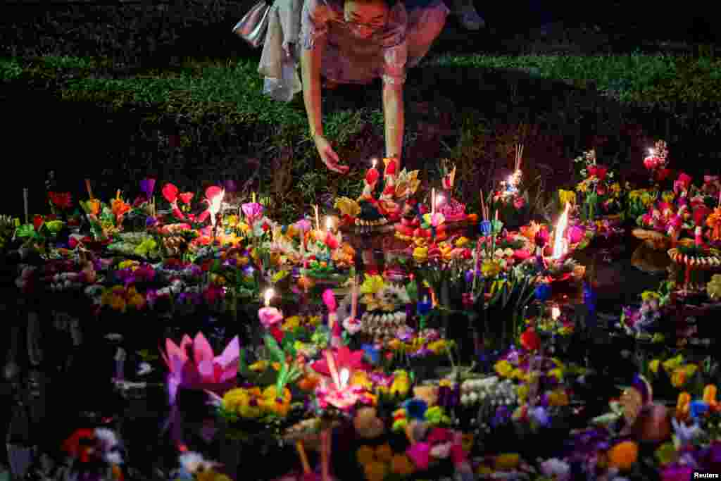 A woman places a Krathong, a floating basket made with leaves and flowers, into a park&#39;s lagoon during the Loy Krathong festival, a symbolic apology and expression of gratitude to the goddess of the river for the water, in Bangkok, Thailand.