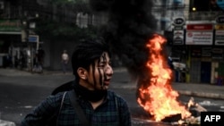 A protester with his face painted stands near a burning makeshift barricade during a protest against the military coup, in Yangon, March 30, 2021. 