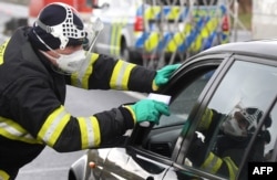 FILE - A Czech special police officer, with a protective mask, checks the temperature of a driver at the border crossing between Germany and Czech Republic, in a measure to protect against the spread of the coronavirus, March 9, 2020.