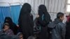 FILE - Two women, center, reportedly wives of Islamic State (IS) group fighters, wait with other women and children at a camp of al-Hol in al-Hasakeh governorate in northeastern Syria, Feb. 7, 2019.