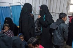 FILE - Two women, center, reportedly wives of Islamic State (IS) group fighters, wait with other women and children at a camp of al-Hol in al-Hasakeh governorate in northeastern Syria, Feb. 7, 2019.