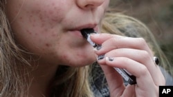 FILE - A high school student uses a vaping device near a school campus in Cambridge, Massachusetts. 