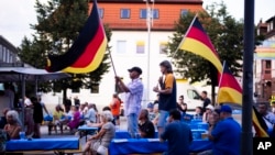 FILE - Supporters of the far-right Alternative for Germany party, or AfD, hold German national flags as they attend an election campaign rally of the party for upcoming state elections, in Suhl, Germany, Aug. 13, 2024.