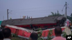 La gente mira los restos destrozados de los dos trenes de pasajeros que descarrilaron el viernes en el distrito de Balasore, en el estado oriental de Orissa, India, el domingo 4 de junio de 2023.