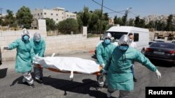 Personal médico palestino carga el cuerpo de una persona fallecida a causa del coronavirus para ser enterrado en un cementerio en Hebrón. 29 de junio de 2020.