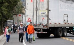 Residents walk along the Pan-American highway blocked by semi-trailer trucks during a nationwide strike that shut down taxi, bus and other services in response to a sudden rise in fuel prices, in Cangahua, Ecuador, Oct. 4, 2019.