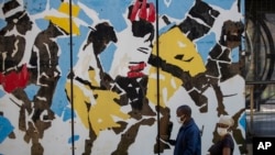 People wearing face masks as a precaution against the spread of the coronavirus, walks past a painting at a bus station in downtown Johannesburg, South Africa, Thursday, May 7, 2020. South Africa begun a phased easing of its strict lockdown measures…