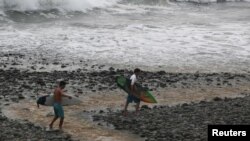 ARCHIVO - Los surfistas caminan por el agua en la playa de El Tunco en Tamanique, El Salvador.Agosto 1 de 2017.