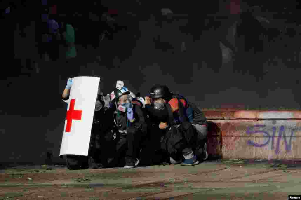 Members of a first aid team and a photographer take cover during an anti-government protest in Santiago, Chile, Oct. 28, 2019.
