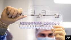 In this March 2021 photo provided by Pfizer, a technician inspects filled vials of the Pfizer-BioNTech COVID-19 vaccine at the company’s facility in Puurs, Belgium.