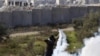 A Palestinian stone-throwing protester uses a sling to throw back a tear gas canister fired by Israeli security officers (rear) during clashes in the West Bank village of Bilin near Ramallah, January 4, 2013. 