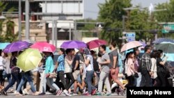 올들어 처음 폭염주의보가 내려진 서울에서 20일 경복궁 앞을 지나는 시민들이 양산과 옷을 뒤집어 쓴 채 걸어가고 있다.