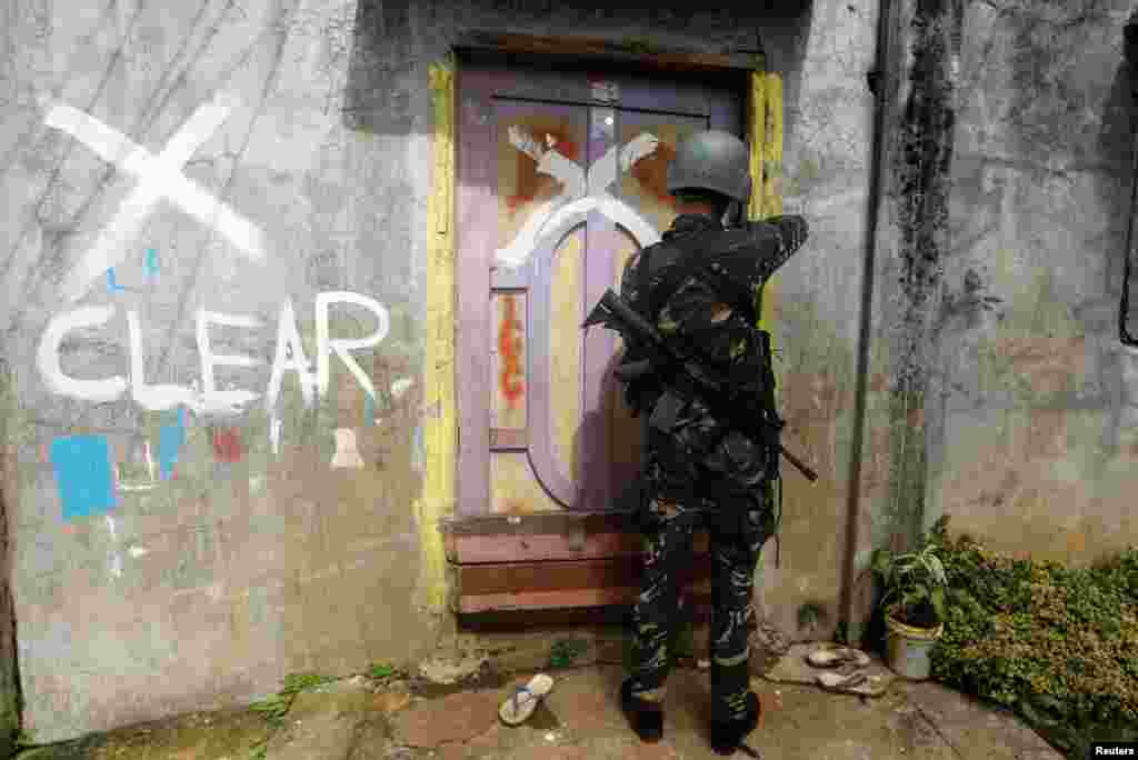 A member of the Philippine National Police closes a door after marking a house as clear while government troops continue their assault against insurgents from the Maute group in Marawi city.
