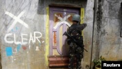 FILE - A member of the Philippine National Police (PNP) closes a door after marking a house as clear while government troops continue their assault against insurgents from the Maute group in Marawi city, June 29, 2017.